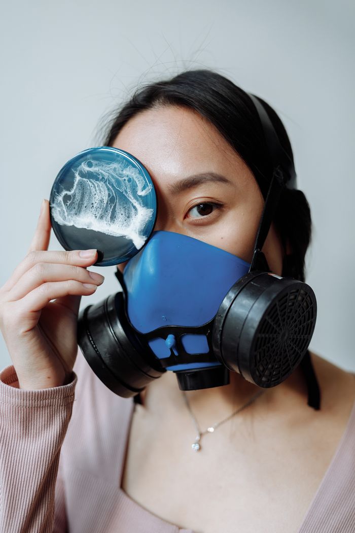 Creative portrait of a woman wearing a respirator mask, holding resin art piece.